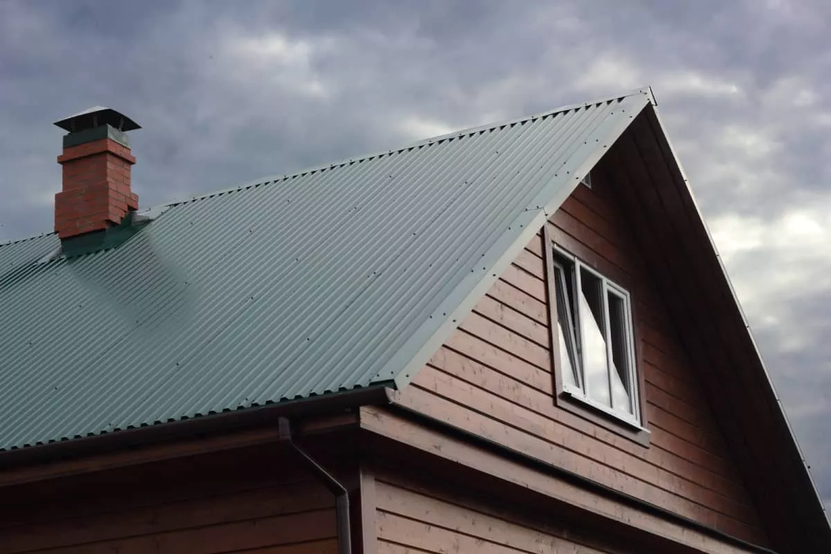 A Kyle metal roof on a wooden house with a chimney under cloudy sky.