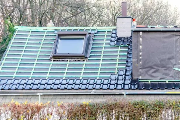 Round Rock Roofers working on a green and black tiled roof with skylight.