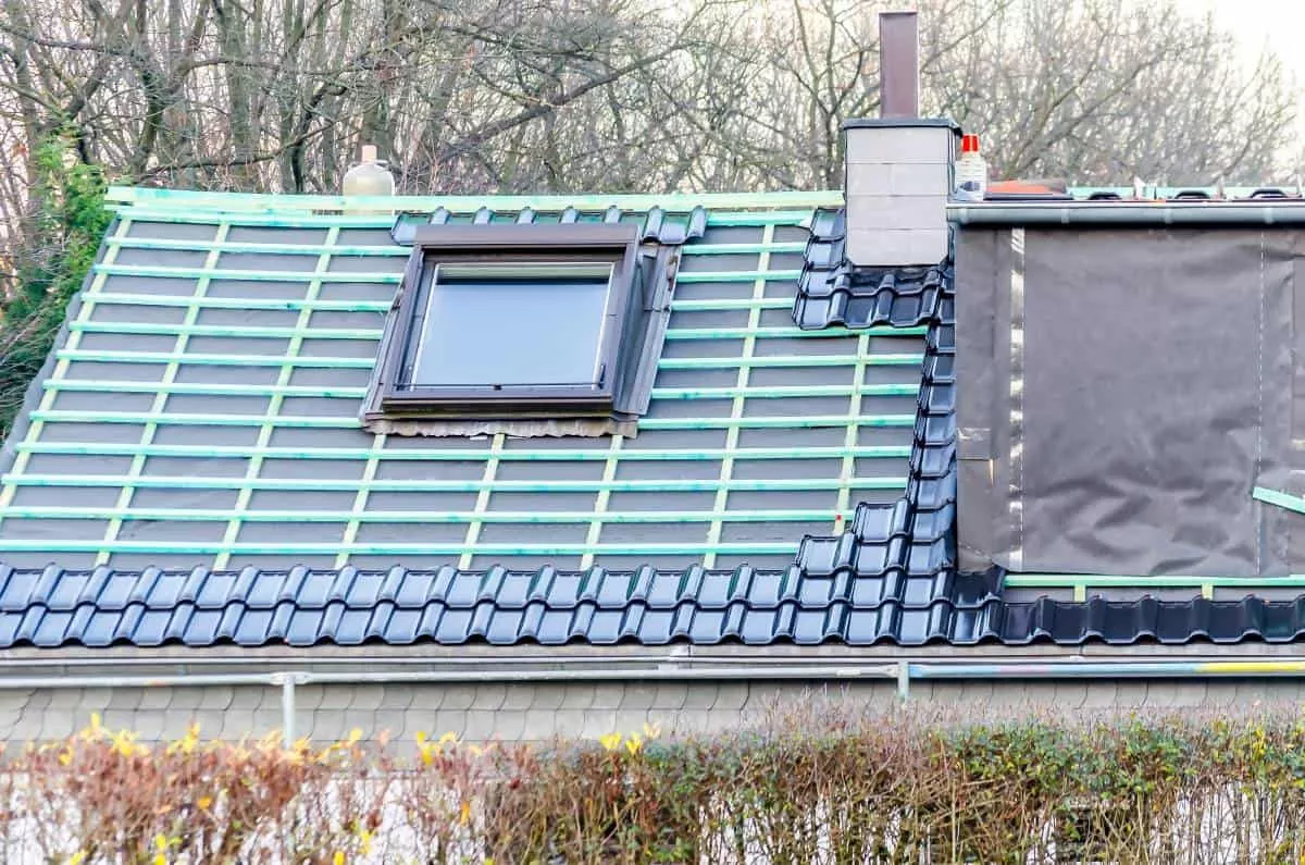 Round Rock Roofers working on a green and black tiled roof with skylight.