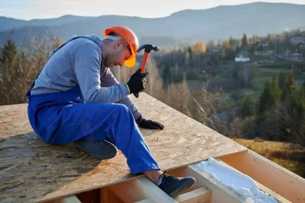 Worker hammering on a roof, showcasing New Braunfels roofing with scenic backdrop.