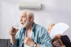 A man drinking water and a woman with fan that could benefit from a Buda solar installation to keep cool and save money.