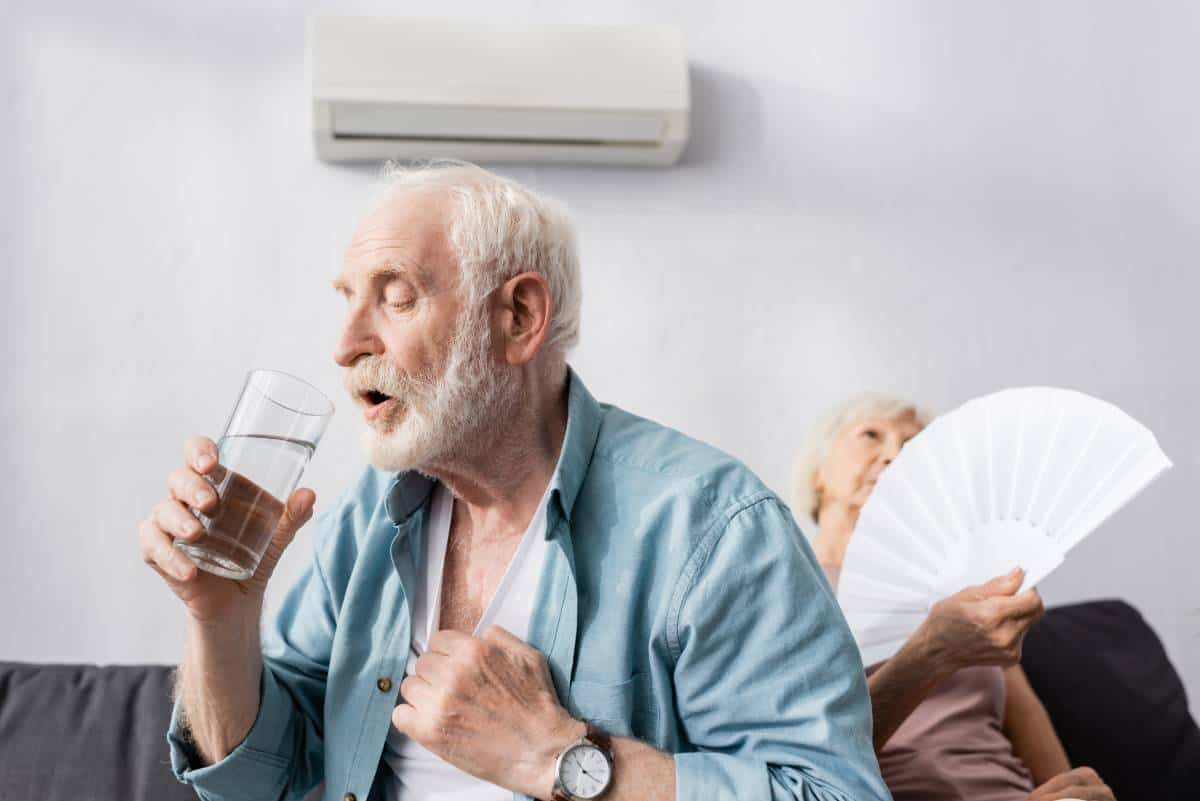 A man drinking water and a woman with fan that could benefit from a Buda solar installation to keep cool and save money.