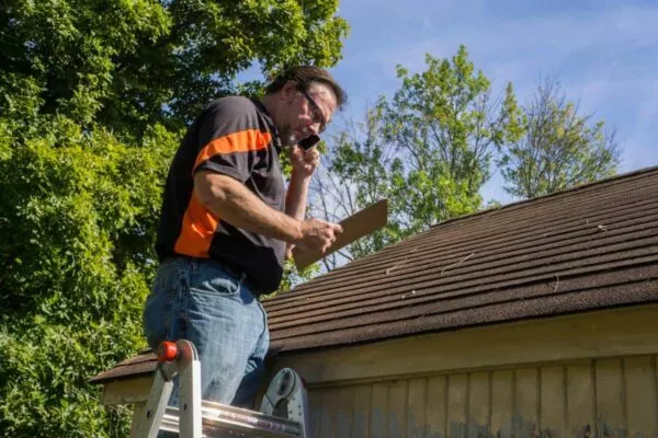 Man inspecting damage for a San Marcos roofing job, standing on ladder with clipboard.