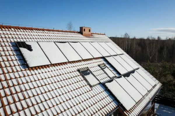 Drone view of solar panels on a house roof, partially covered in snow, showcasing Lockhart roof services during Winter