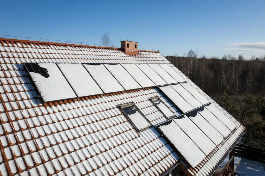 Drone view of solar panels on a house roof, partially covered in snow, showcasing Lockhart roof services during Winter