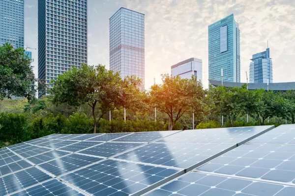 Solar panels sit on a commercial lot with a downtown city skyline as the backdrop.