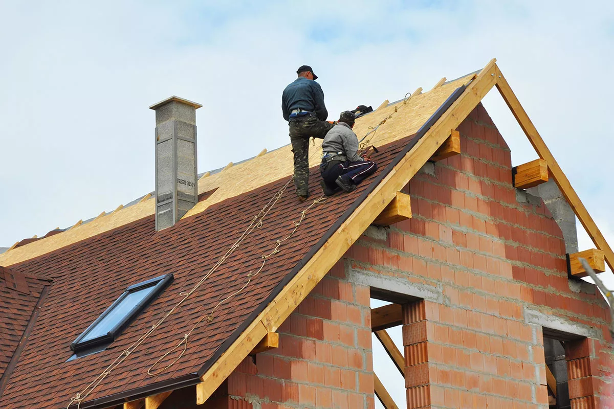 Workers install shingles for New Braunfels roofing on a steep roof.