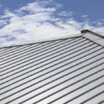 A light colored metal roof with a cool coating sits under a blue sky.