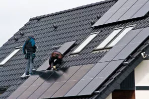 Workers are installing solar panels on a gray metal roof.