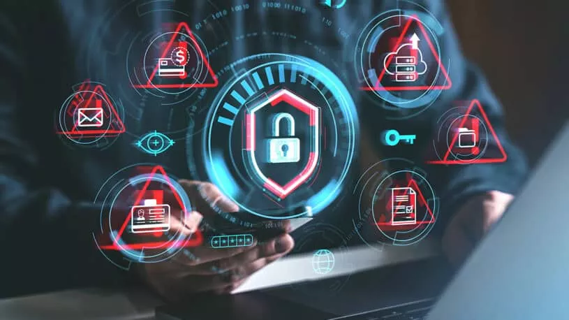 A person holds a smartphone with digital security icons displayed around, including a padlock, alert symbols, and various data protection graphics, set against a blurred laptop.