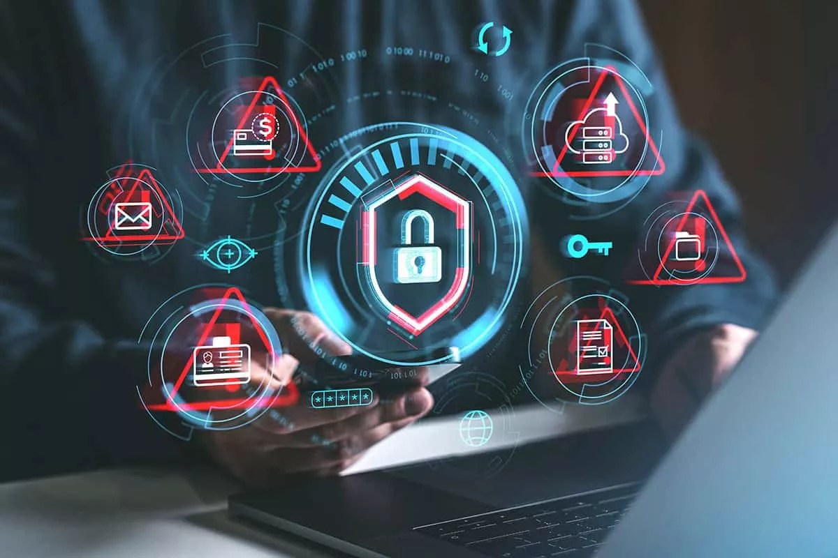 A person holds a smartphone with digital security icons displayed around, including a padlock, alert symbols, and various data protection graphics, set against a blurred laptop.