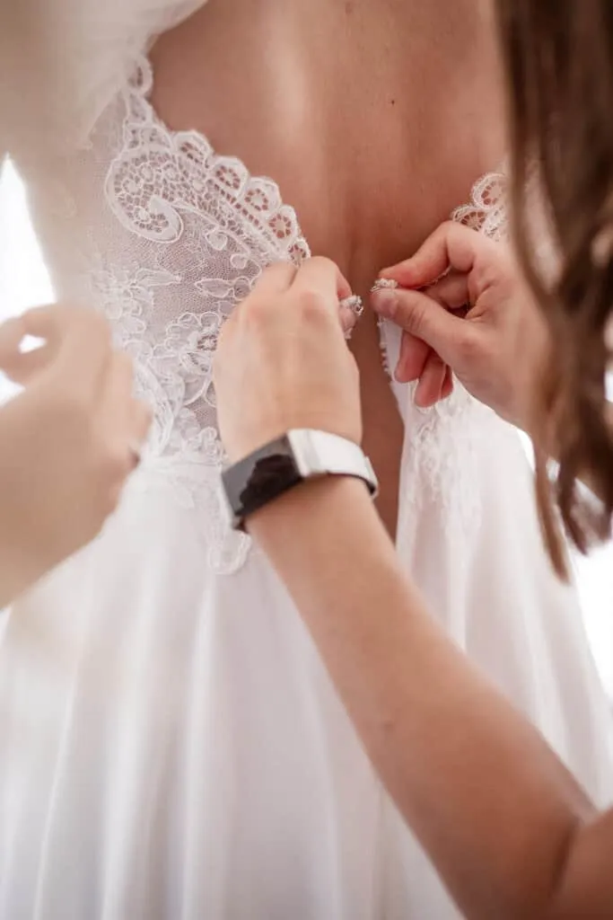 Frau schließt das Hochzeitskleid mit Spitze am Rücken.
