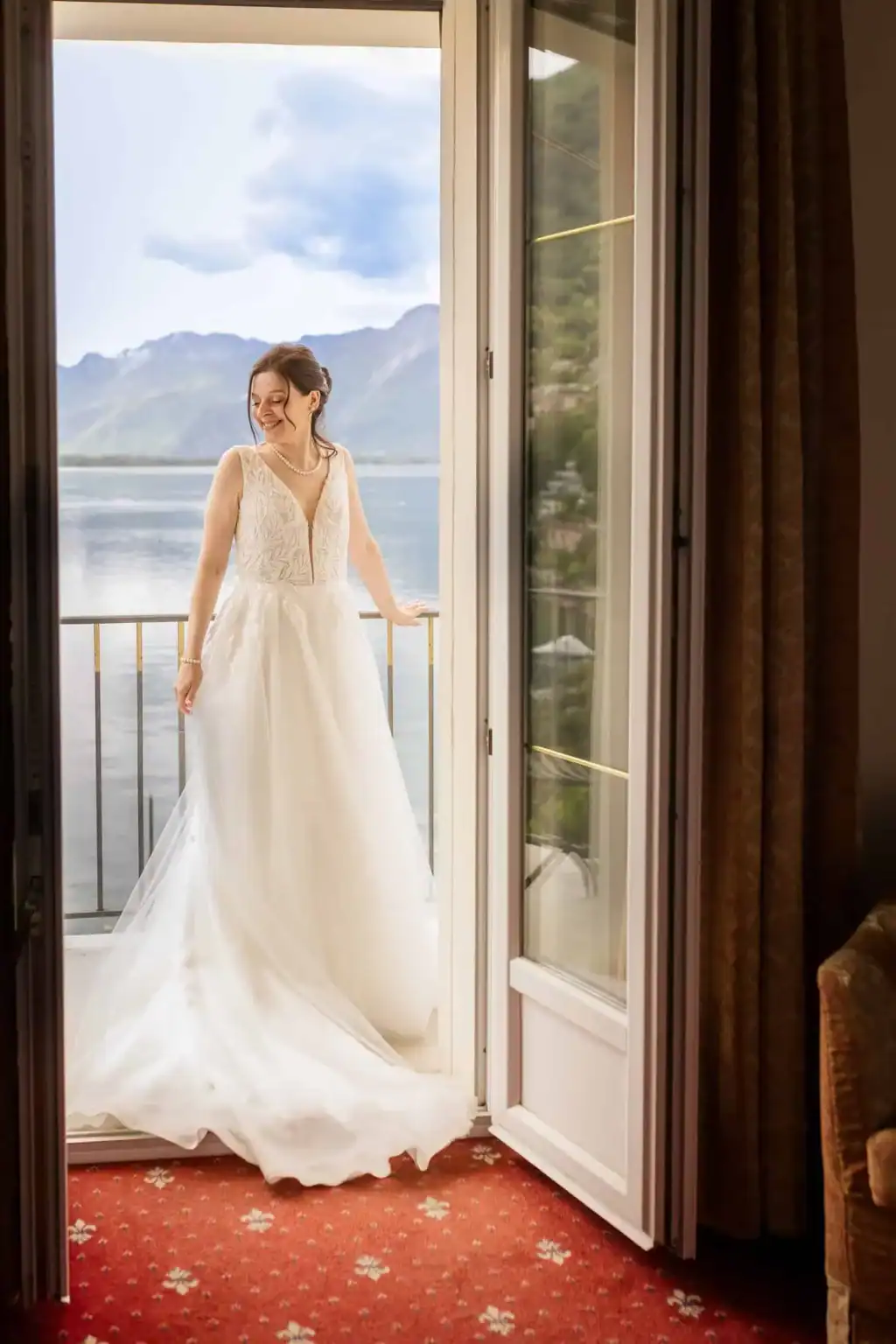 Hochzeitsfotograf buchen - Braut auf dem Balkon mit Blick auf See und Berge – elegante, natürliche Hochzeitsfotografie