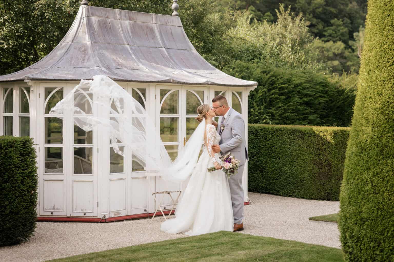 Hochzeitspaar vor einem weißen Pavillon im Garten, romantische Atmosphäre, Natur und Liebe.