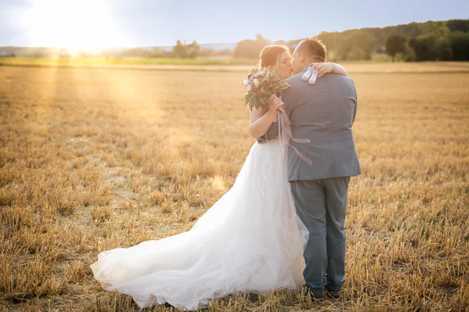 Romantisches Hochzeitsfoto im Feld bei Sonnenuntergang, emotionale Momente zwischen Braut und Bräutigam.