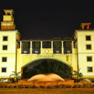 A well-lit, ornate building with "HIALEAH" inscribed above an arch at night, near a renowned printing service in Hialeah. The structure includes two clock towers flanking the arch, with a fountain in the foreground and surrounding greenery, highlighting its architectural elegance.