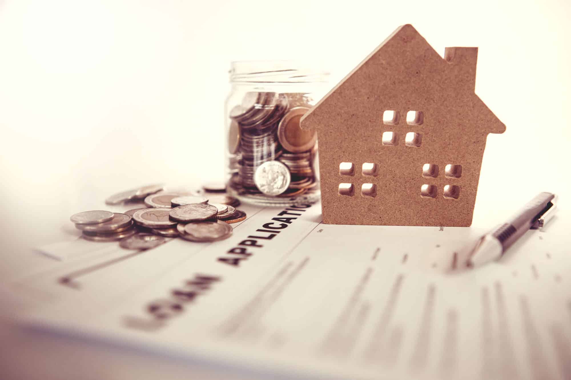 loan application paper with coins, a pen, and a house-shaped paper on top of it