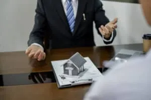 A real estate agent with a House model is talking to clients abo