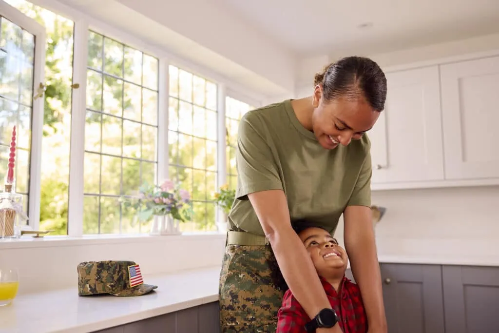 American Army Mother In Uniform Home On Leave Hugging Son In Family Kitchen