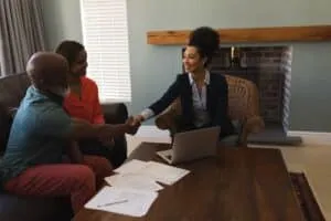 Front view of a female real estate agent shaking hands with a senior man while sitting in the living room at home
