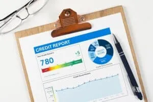 A credit report on a clipboard shows a credit score of 780, charts, graphs, and a pen next to the report—ideal details for anyone considering a Mortgage Co-Signer. Glasses are also visible in the upper left corner.