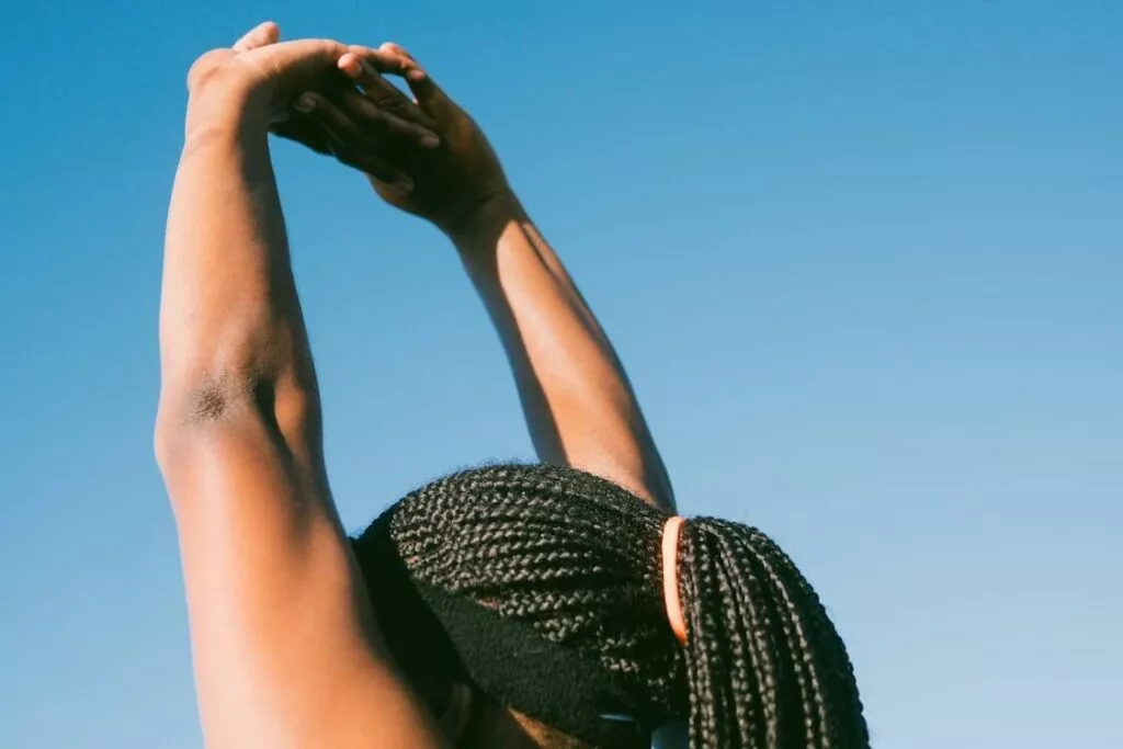 Person with braided hair stretching arms under a blue sky.