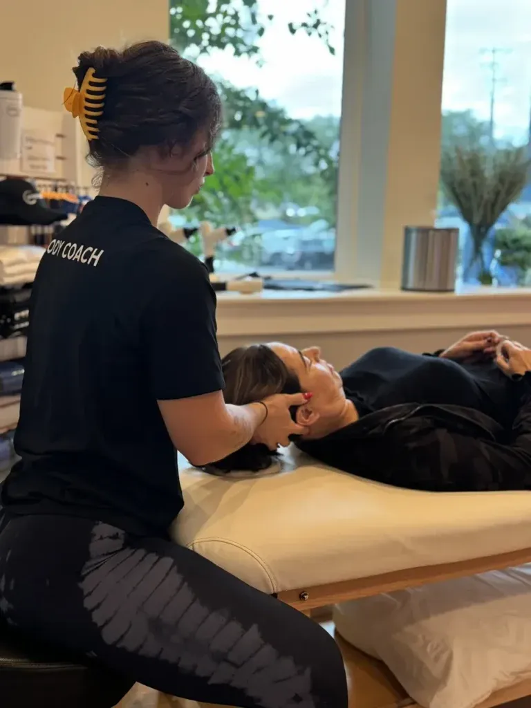 Wellness coach gives treatment on a massage table near a sunny window.