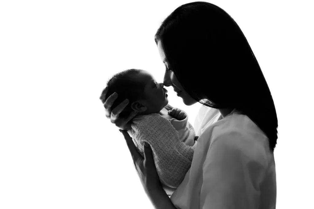 A woman holds a baby close to her face, both shown in silhouette against a white background.