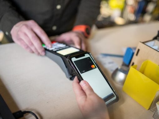 Close-up of woman making payment through NFC. Woman pays via payment terminal and mobile phone. Cashier hand holding credit card reader machine while client holding phone for NFC payment