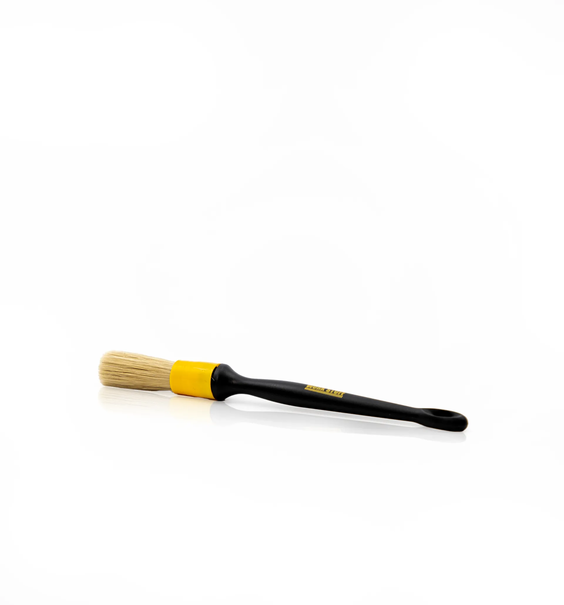 Black-handled brush with beige bristles and yellow ferrule rests on a white surface next to a gray microfiber towel.