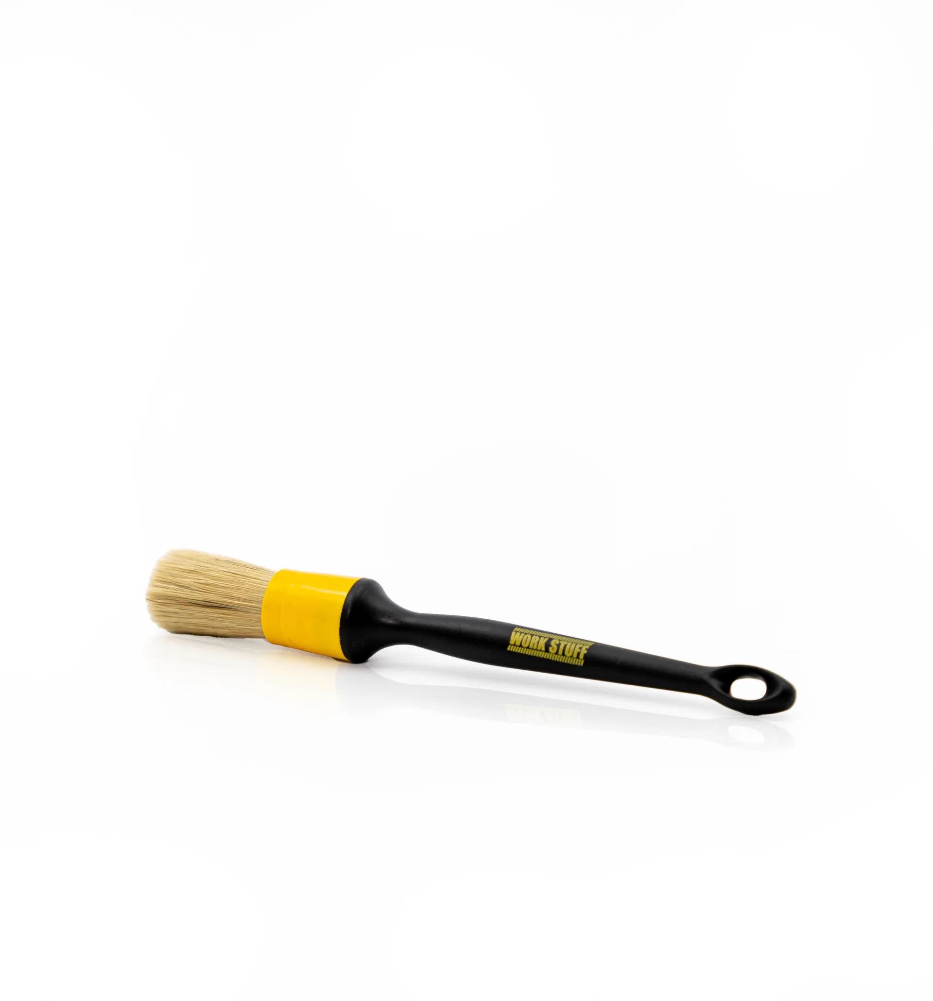 Paintbrush with beige bristles, yellow ferrule, and black handle with hole at end, lying on a white background.