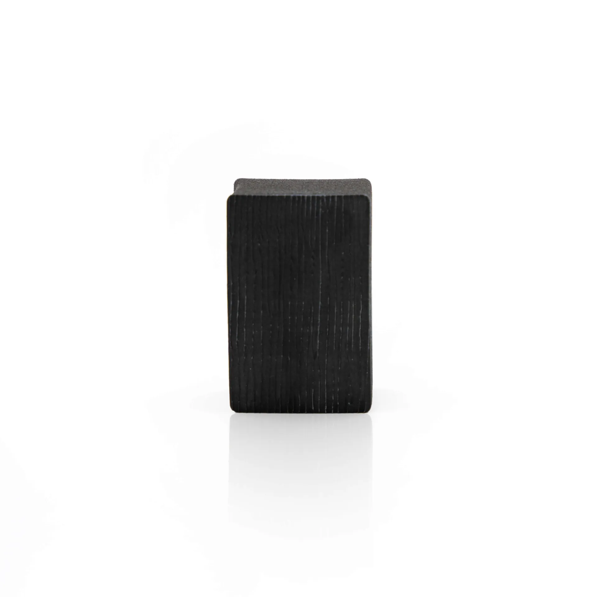 A single rectangular black wooden block stands upright on a white background, casting a faint shadow below.