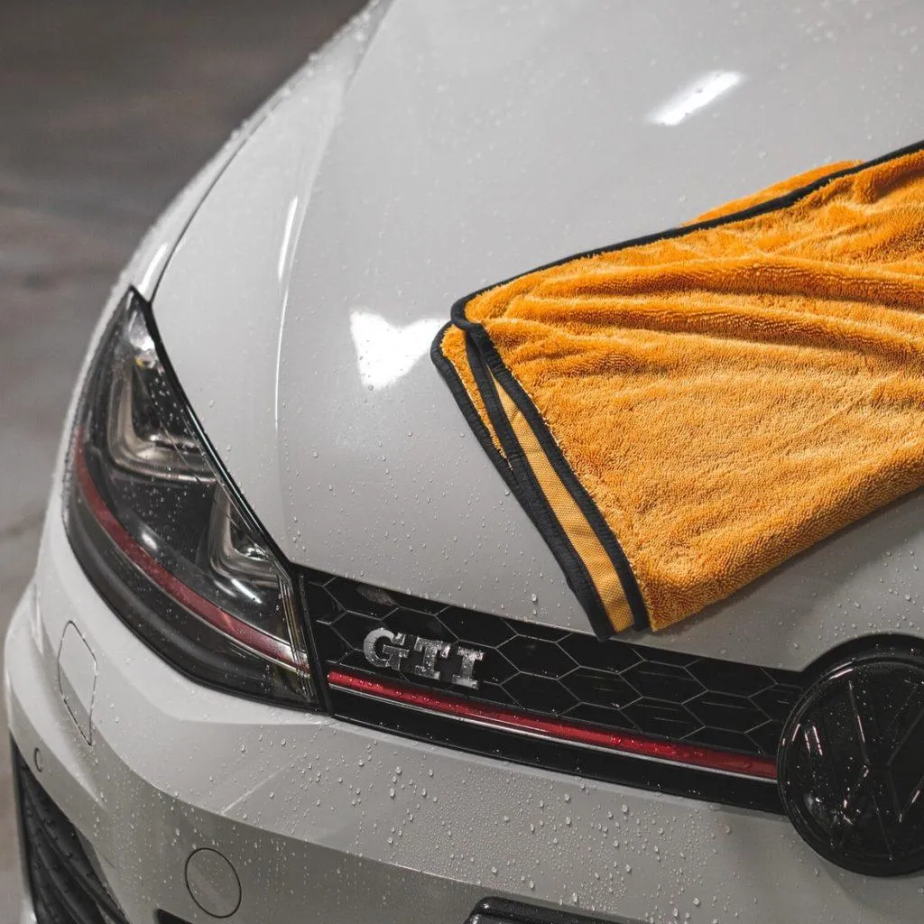 Close-up of a white Volkswagen GTI’s hood with water droplets and an orange microfiber towel partially covering the emblem.