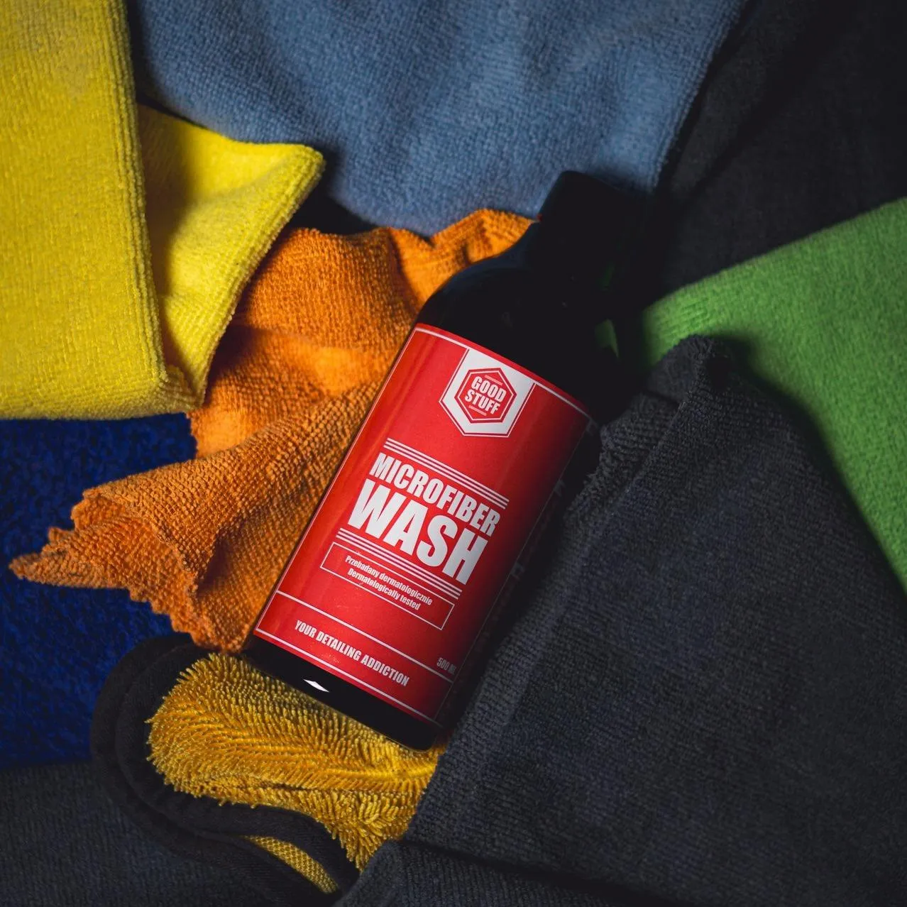 A bottle of Good Stuff Microfiber Wash rests on colorful microfiber towels, including a drying and car detailing towel.