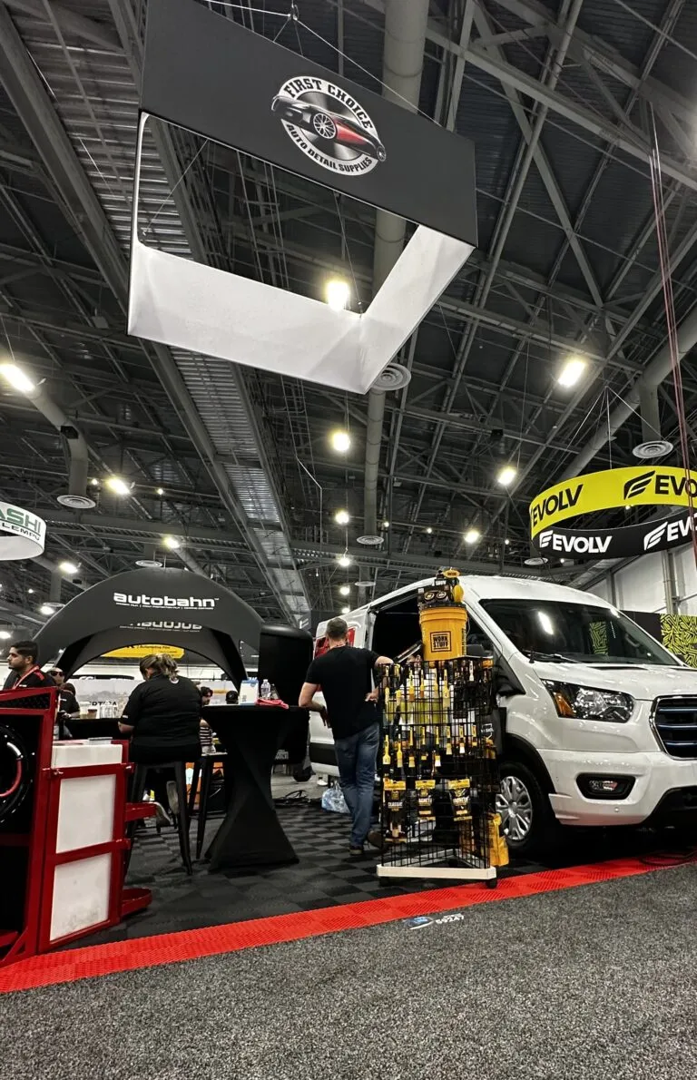 Trade show booth with a white van, tool racks, people at a table, and signs reading EVOLV and Autobahn overhead.