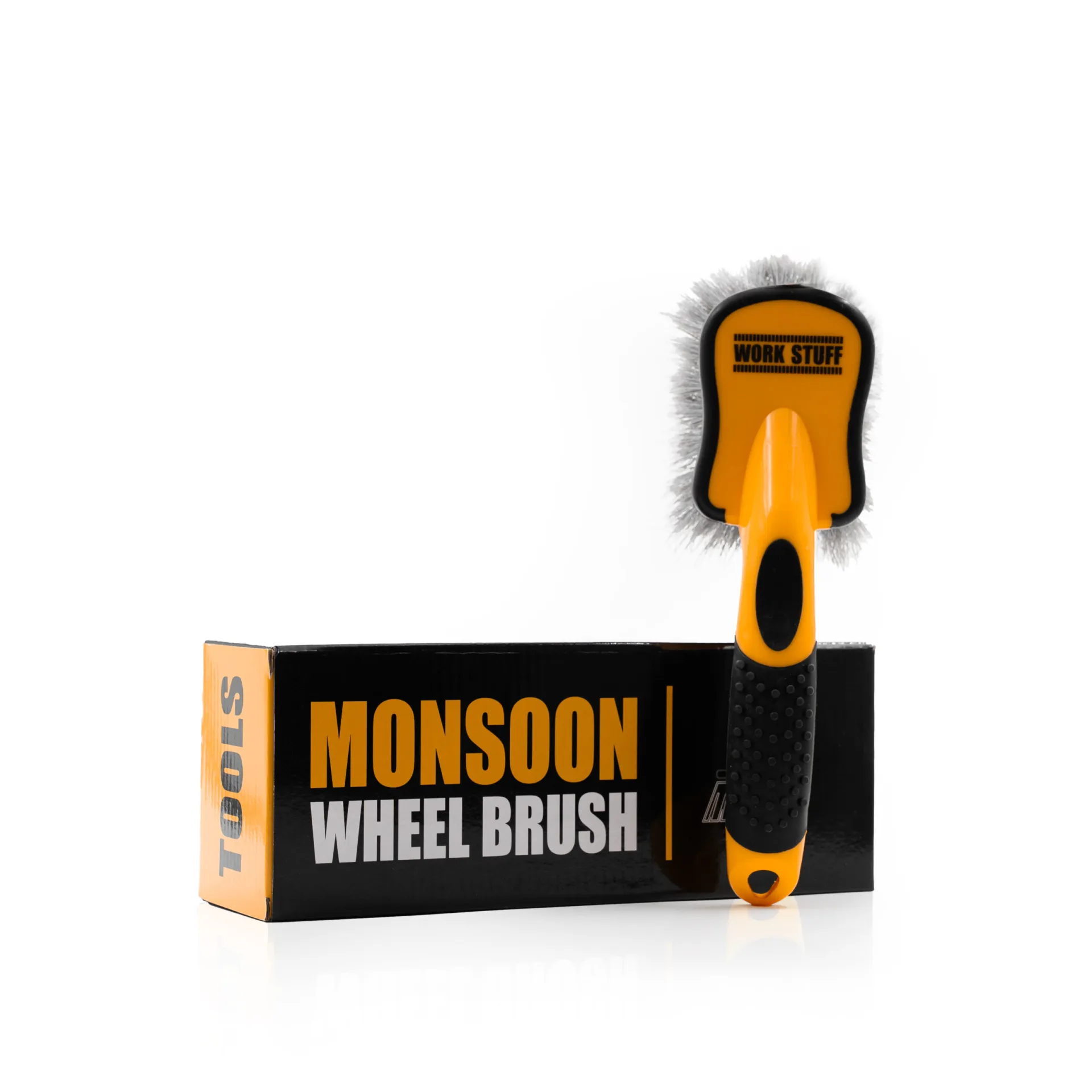 Yellow and black Work Stuff wheel brush stands on a black box with orange Monsoon Wheel Brush text, beside a gray towel.