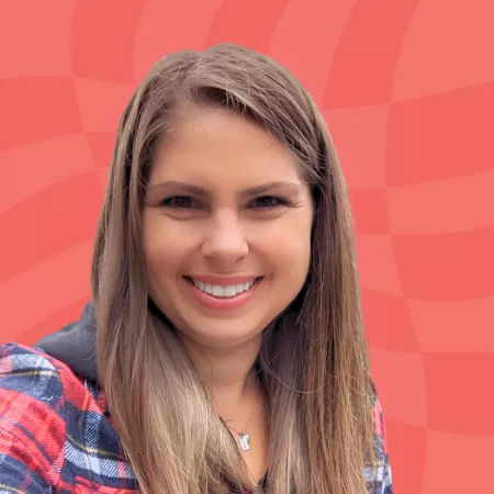 Smiling person with long brown hair wearing a plaid shirt poses against a red textured background.