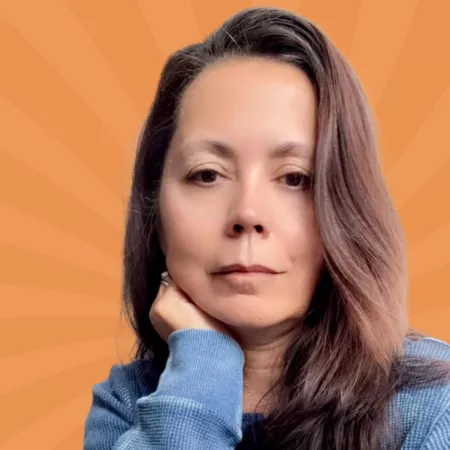 Woman with long brown hair resting her chin on her hand, wearing a blue sweater, against an orange background with sunburst pattern.