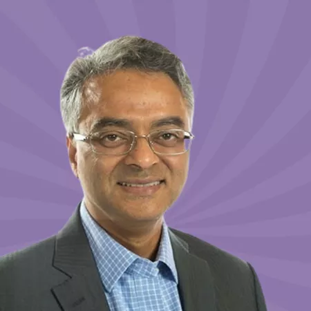 A person wearing glasses and a suit smiles against a purple background with a radial pattern.