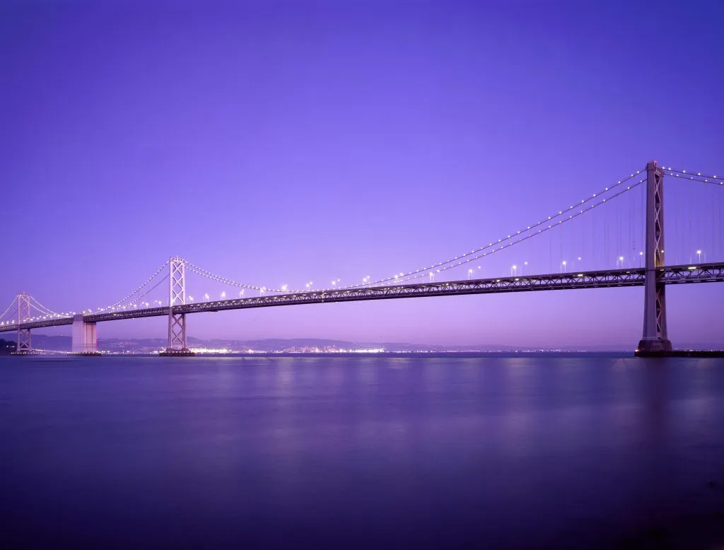 Beautiful view of the Bay Bridge lit up at twilight against a vibrant purple sky.