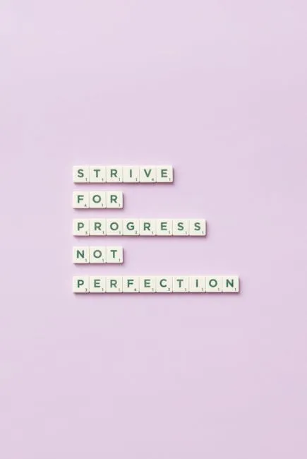 Scrabble tiles spelling 'Strive for progress, not perfection' on a pastel background.