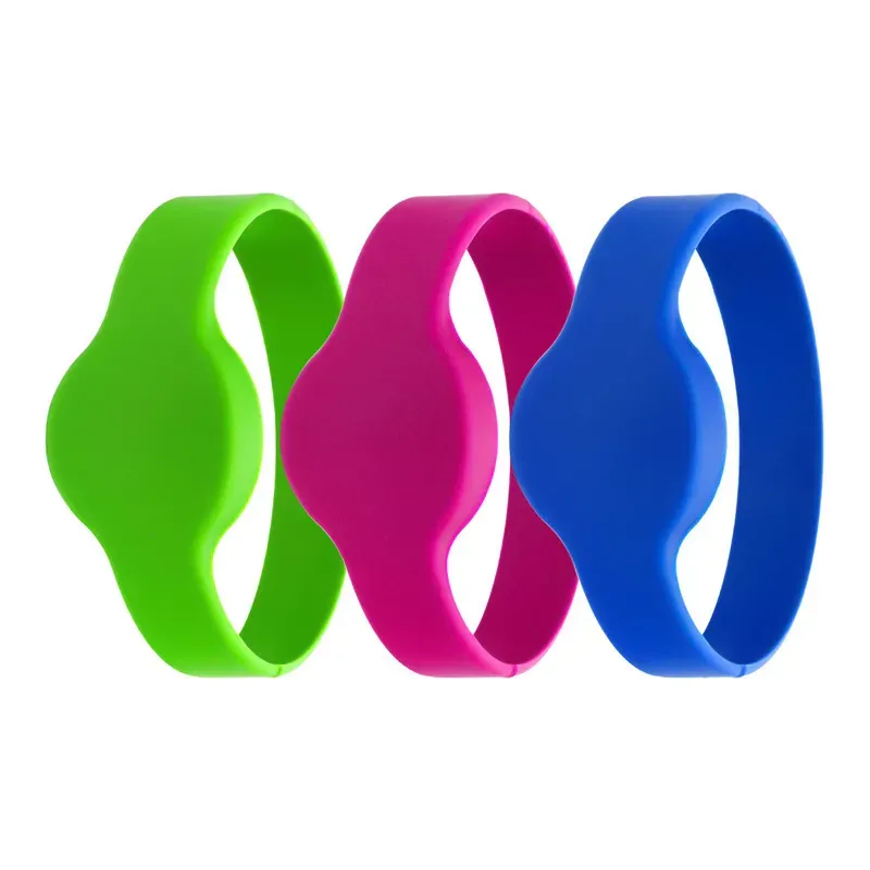 Tres pulseras de proximidad, disponible en verde, rosa, y azul, se muestran en una fila. Cada pulsera de silicona presenta un diseño ondulado en el centro..