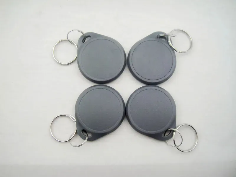 Awọn Fobs Key Igbohunsafẹfẹ Meji mẹrin pẹlu awọn oruka bọtini irin, kọọkan ni grẹy, ti wa ni ṣeto ni a meji-nipasẹ-meji akoj lori kan funfun dada.
