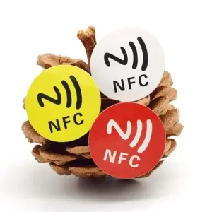 Three NFC Labels in yellow, white, and red are affixed to a pinecone.