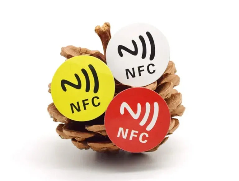 Three NFC Labels in yellow, white, and red are affixed to a pinecone.