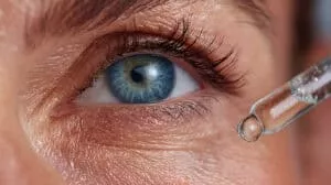 Close up view of a pipette delivering eye drops to a woman's vibrant blue eye, enhancing eye health and promoting clear vision with a soothing moisturizing serum
