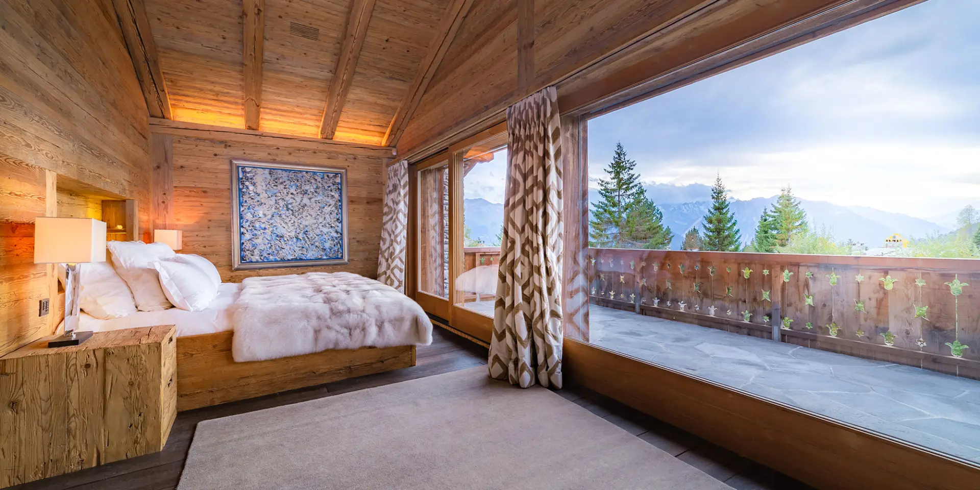 LEE_Image_Stay_1 Luxury GuestLee Geneva villa bedroom with wood accents, plush bed, fur blanket, Alps view balcony, modern décor, warm lighting. | GuestLee luxury rental Switzerland