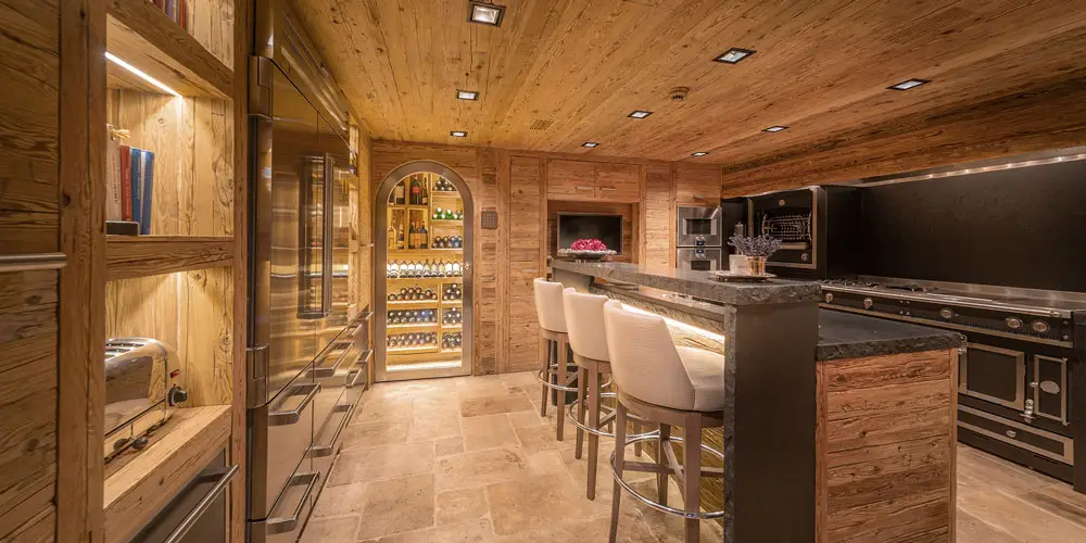 LEE_Image_Stay_2 Luxury Verbier chalet kitchen & wine cellar at GuestLee, with wood accents, marble island, and glass wine wall for upscale rentals. | GuestLee luxury rental Switzerland