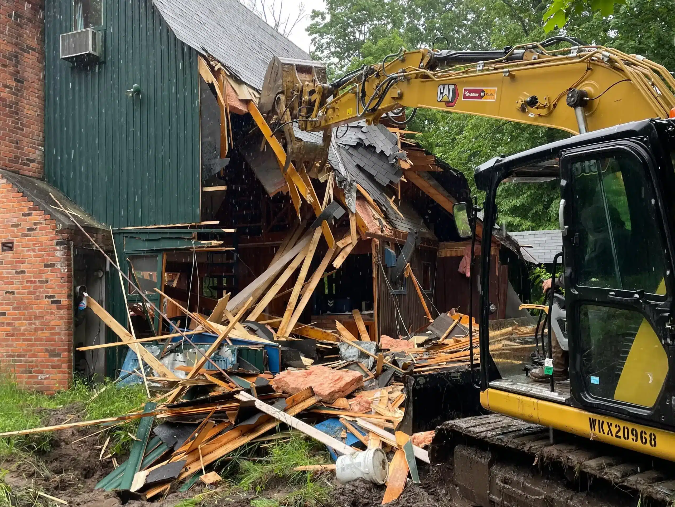 A yellow excavator demolishes part of a wooden building, with debris and broken beams scattered on the ground—expertly handled by excavation contractors DeWitt MI. Kenneth Bros