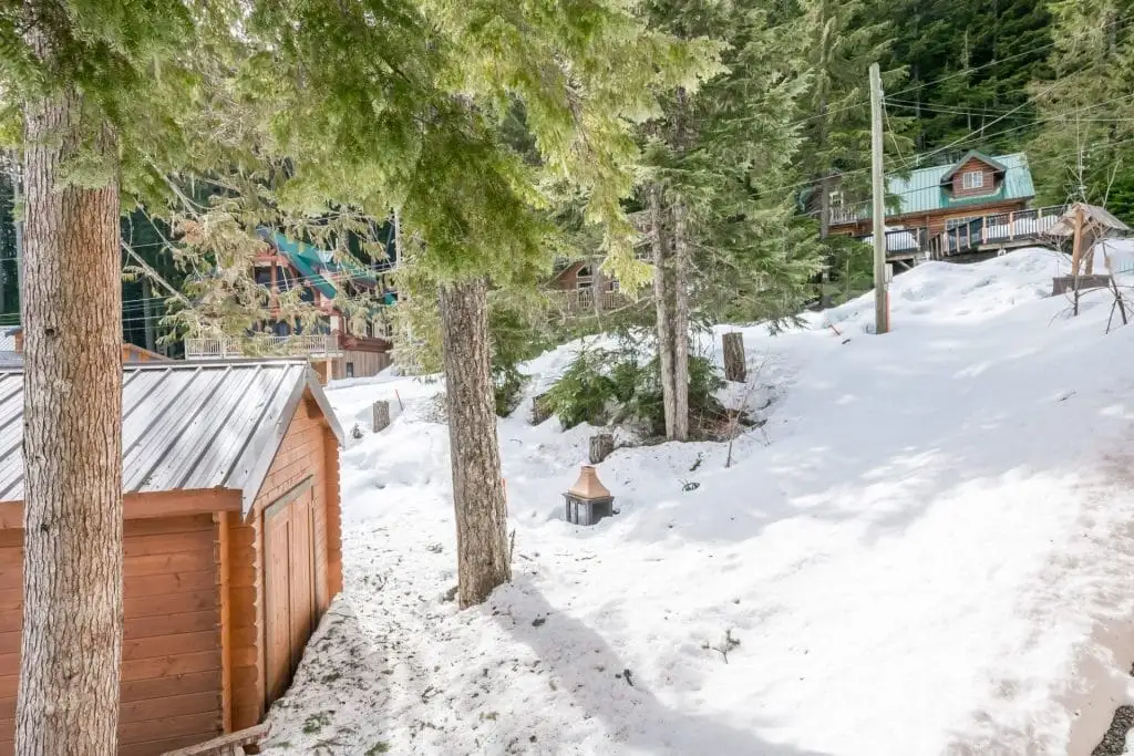 Small wooden cabins and trees dot a snowy hillside, with more cabins and forest in the background—perfect for discovering things to do in Sunshine Valley.